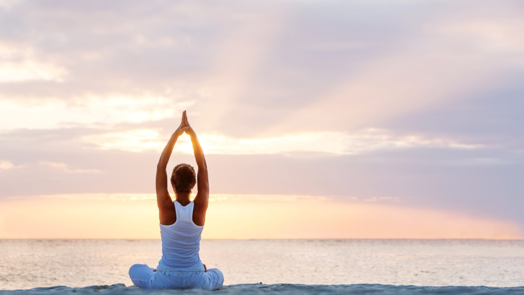 A woman doing yoga on the beach overlooking an early morning horizon.