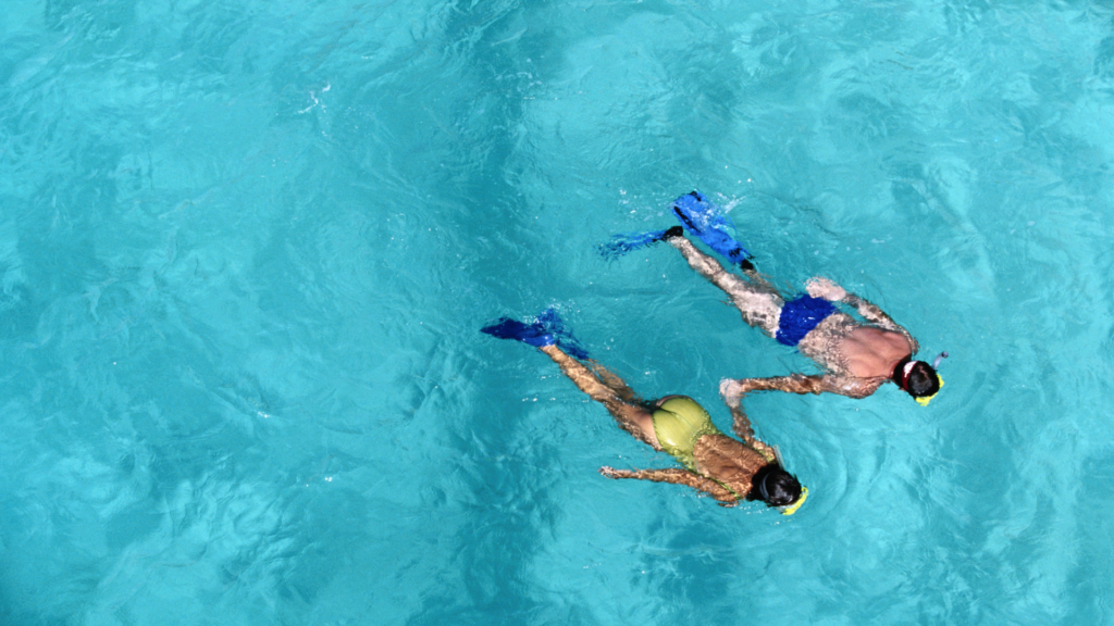 Couple snorkeling together while holding hands in clear blue ocean water.