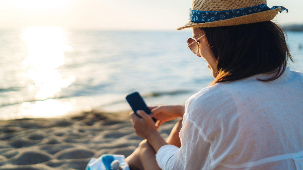 Woman using her phone sitting at the beach.